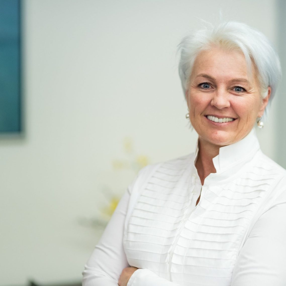 Porträt einer lächelnden älteren Frau mit grauen Haaren in einem hellen Hemd.