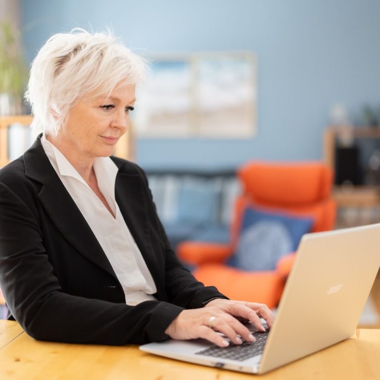 Webinar Online-Mediation Eine Frau schreibt am Tisch, neben ihr ein Laptop, Tasse und Smartphone.