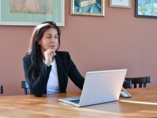 Führungskraft Frau mit langen Haaren sitzt nachdenklich vor einem Laptop in einem hellen Raum.