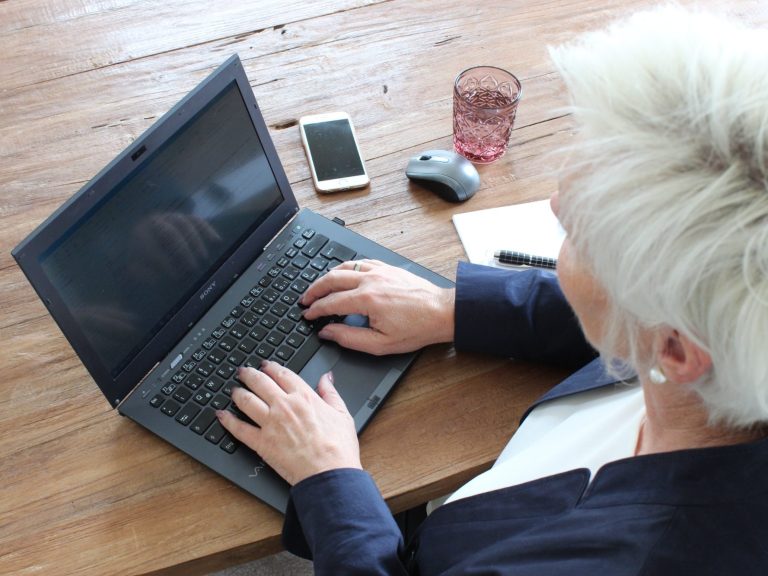 Webinarreihe 4 Eine Person mit grauen Haaren tippt auf einem Laptop auf einem Holztisch.